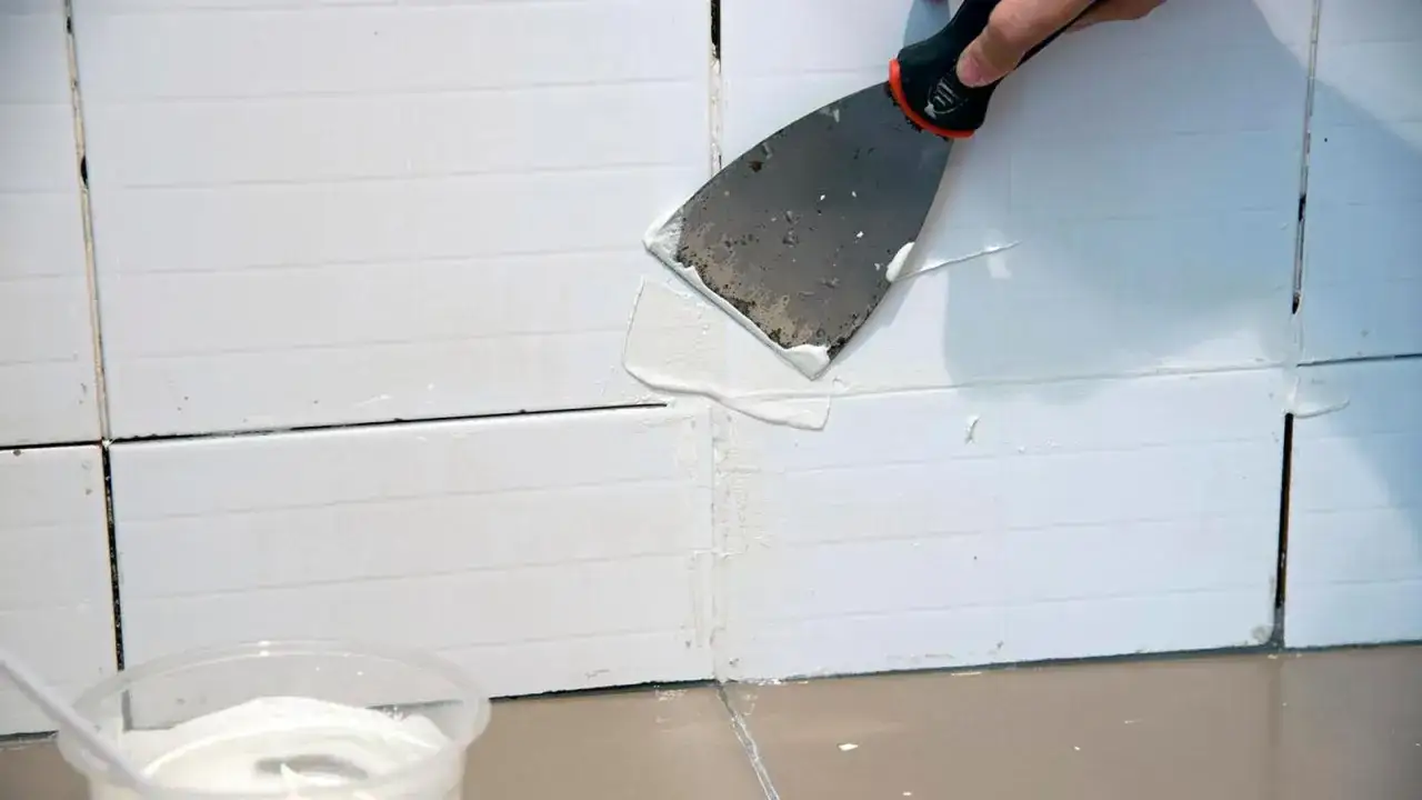 Aplicando masilla blanca con una esp&aacute;tula para rellenar las juntas de baldosas.