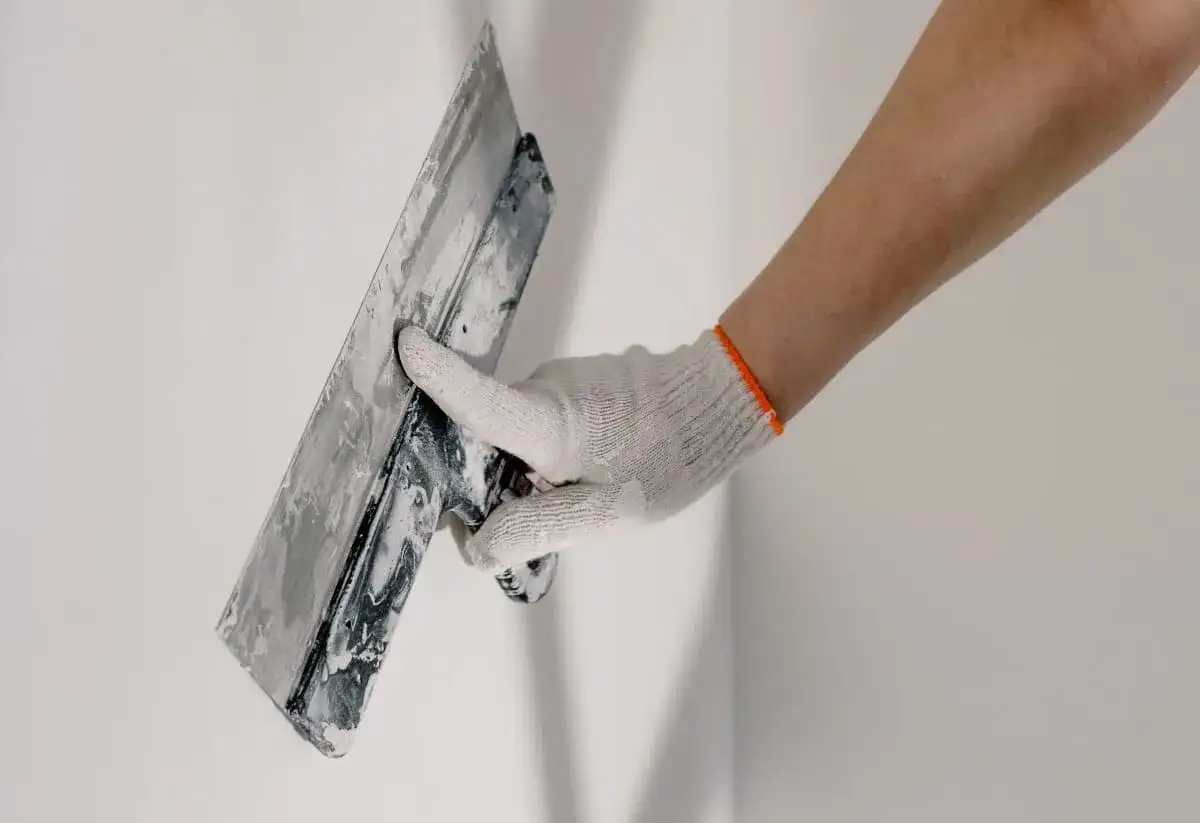 Mano enguantada aplica masilla para revocar pared.