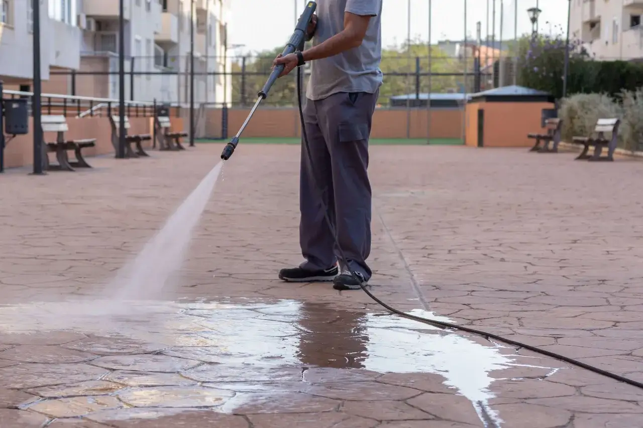 Persona limpia el suelo poroso con una hidrolimpiadora, creando un charco de agua.