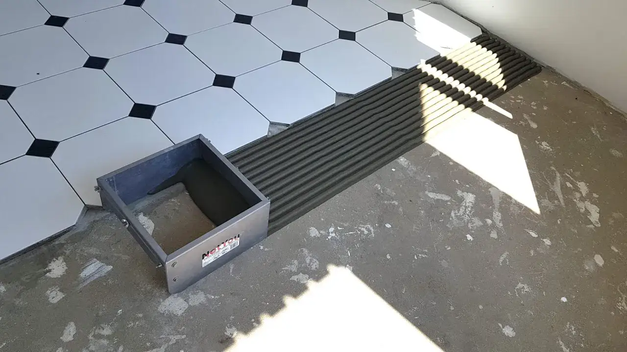 Herramienta para pegar cer&aacute;mica con cemento fresco y baldosas blancas con detalles negros listas para colocar.