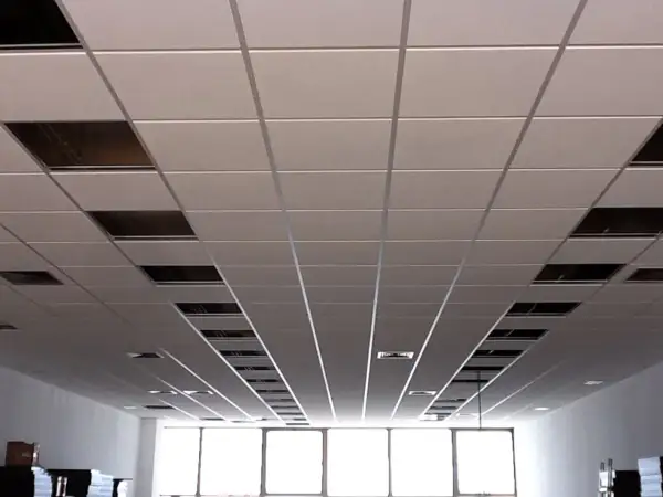 Un plenum falso techo modular con paneles blancos y rejillas metálicas visibles en algunos huecos.