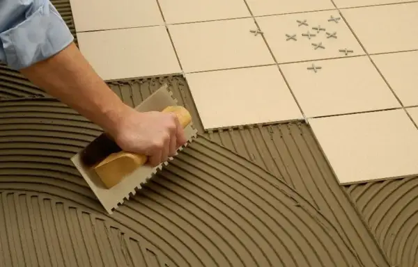 Mano extendiendo cemento cola con llana para poner azulejos.