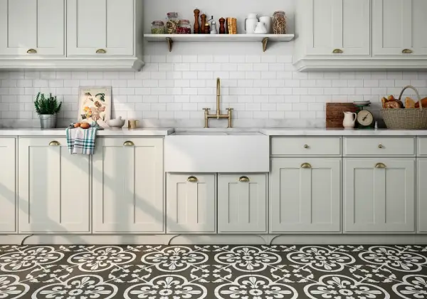 Cocina con suelo hidráulico de diseño floral. Encimera de mármol, fregadero blanco, grifería dorada y armarios claros.