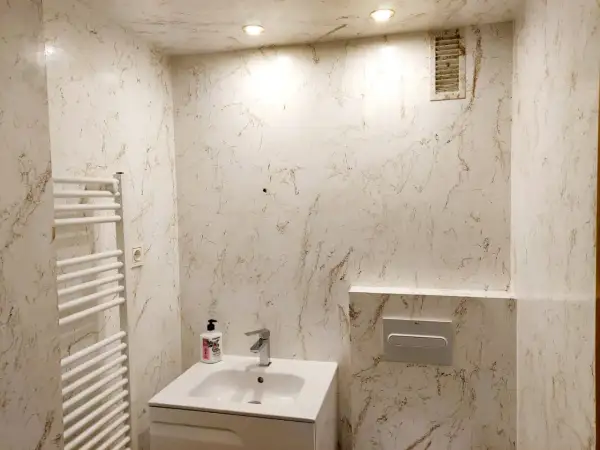 Elegante baño con paredes y techo acabados en resina epoxi con veteado marrón sobre blanco. Incluye lavabo, toallero y cisterna empotrada.