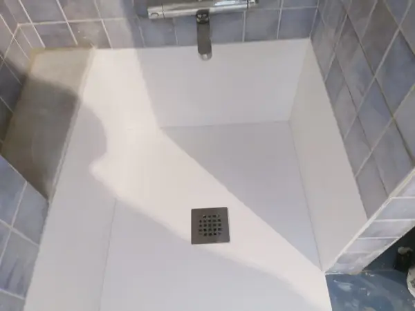 Instalación de un nuevo plato de ducha blanco, con azulejos azules y grifería cromada.