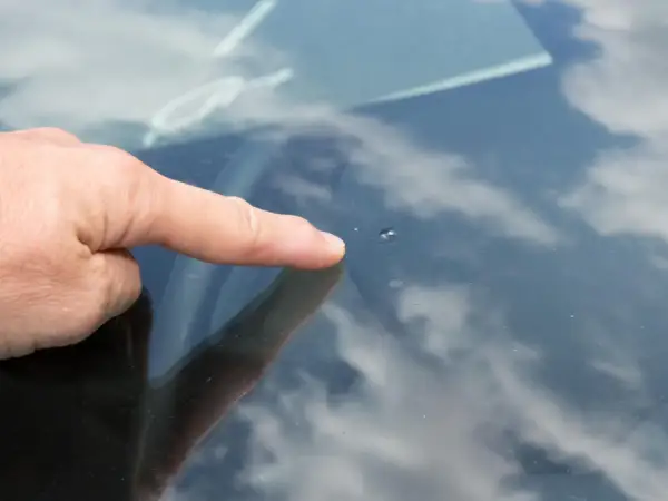 Dedo señala un pequeño impacto en el parabrisas, un cristal manchado por dentro por la suciedad y el reflejo del cielo nublado.