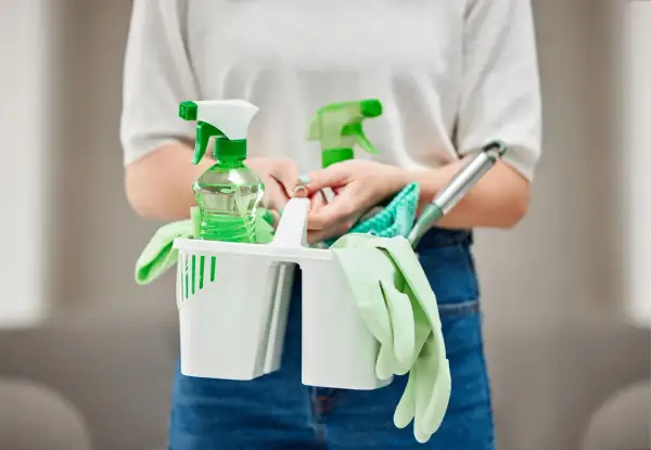 Persona con kit de limpieza: guantes, botellas rociadoras y paños. Las funciones de un auxiliar de limpieza son variadas.