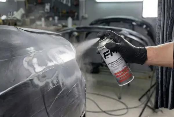 Mano enguantada aplica imprimación en spray a un coche. Se puede dar imprimación encima de pintura para un acabado perfecto.