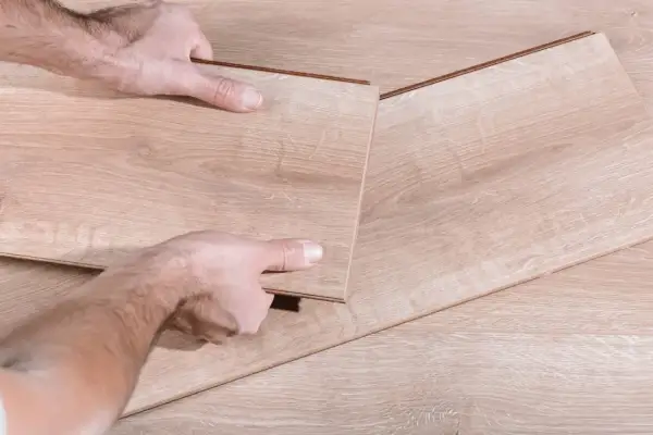 Man's hands fitting a new laminate plank to replace damaged parquet.