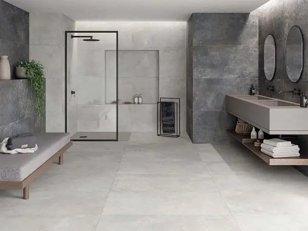 Baño moderno con ducha, lavabo doble y banco. Paredes y suelo revestidos con elegante material gres en tonos grises y oscuros.