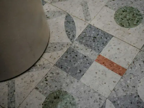 Detalle de un suelo terrazo con diseño geométrico y un pilar. El pulido del suelo terrazo resalta sus motas de colores.