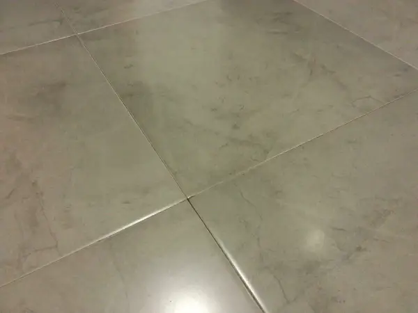 Detalle de la colocación de cerámica gris en un suelo, mostrando las juntas finas y el acabado mate.