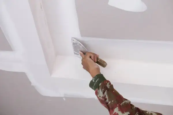 Mano aplica masilla con espátula en el techo, como quitar escayola del techo.